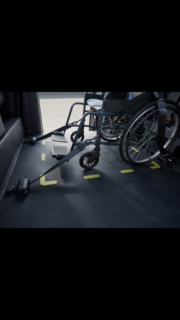 Rollstuhl im Kia PV5 WAV mit vorderem und hinterem Rückhaltesystem für Stabilität während der gesamten Fahrt gesichert.
